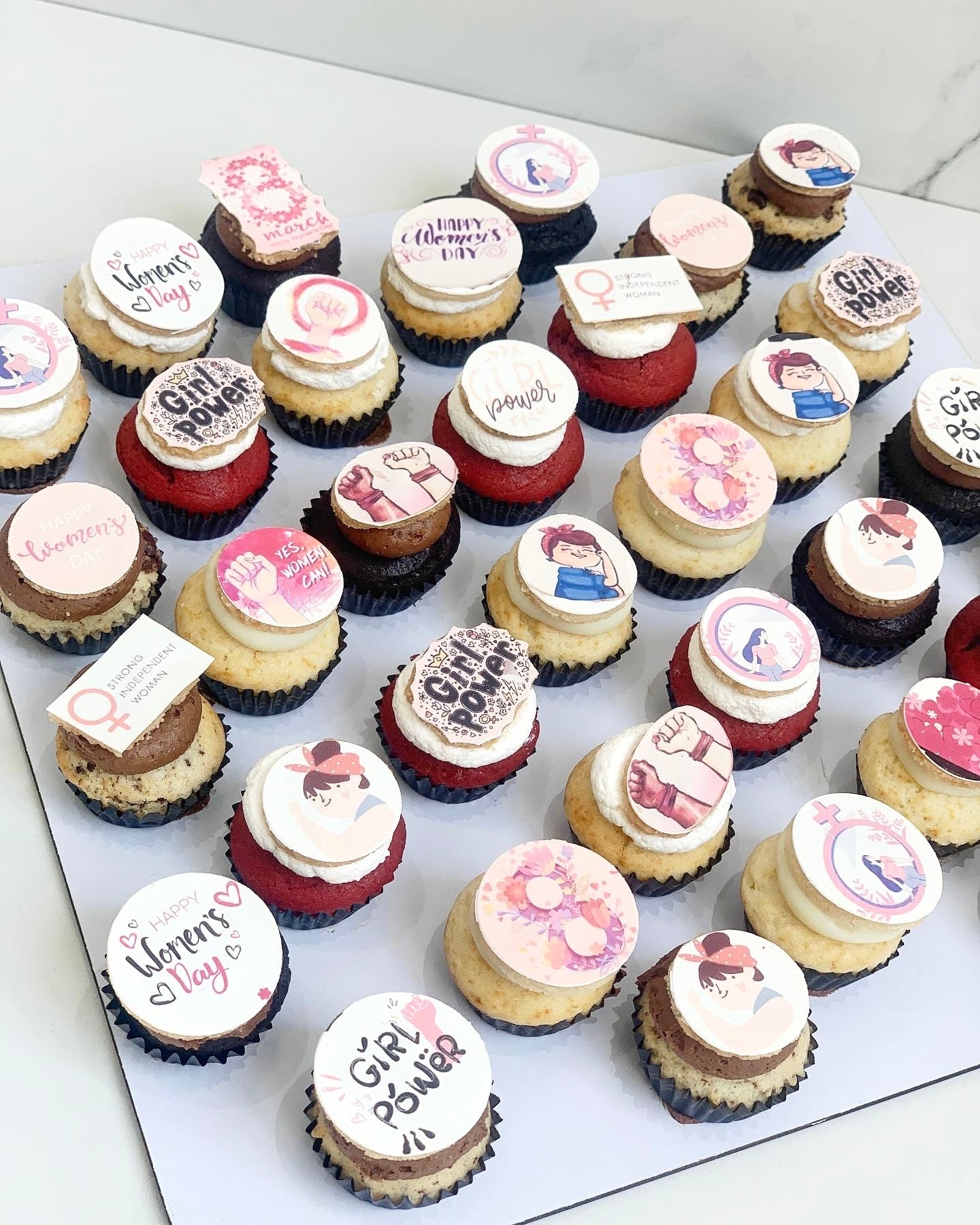 Assorted colorful cupcakes with frosting and sprinkles from The Sinful Spoon on a white plate.