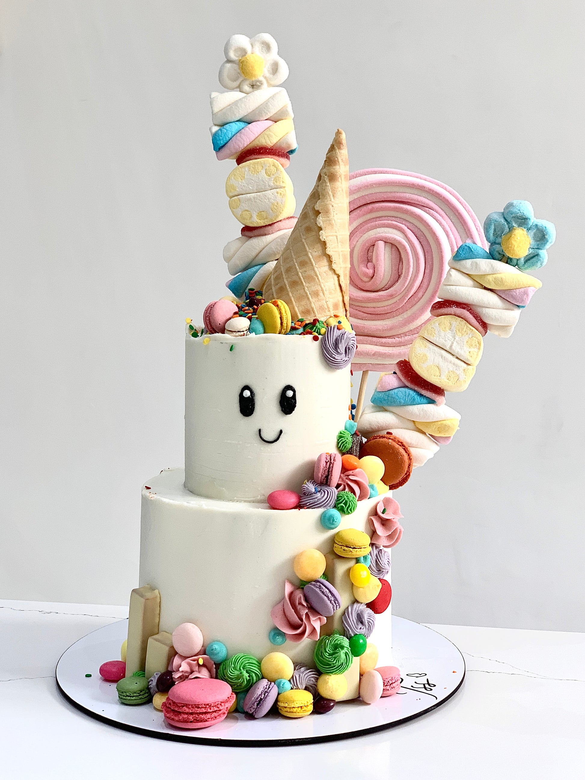 Colorful tiered kids cake from The Sinful Spoon featuring bright frosting and playful decorations on a white background.