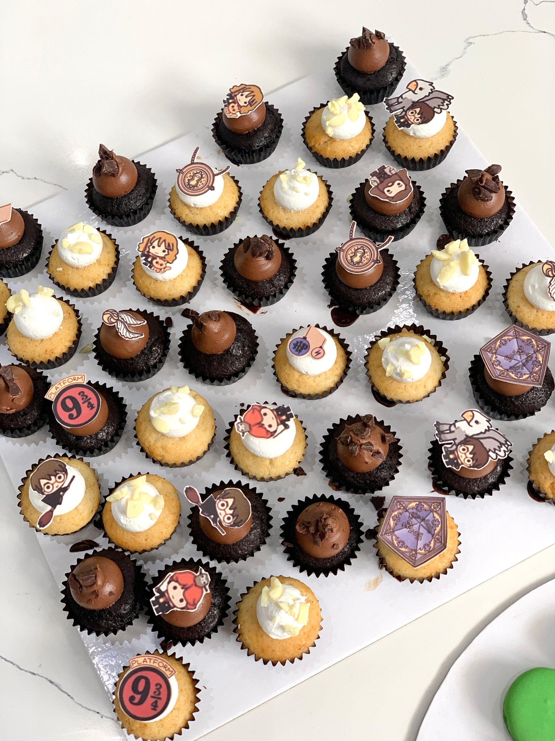 Colorful cupcakes with swirled frosting and sprinkles from The Sinful Spoon on a white plate.