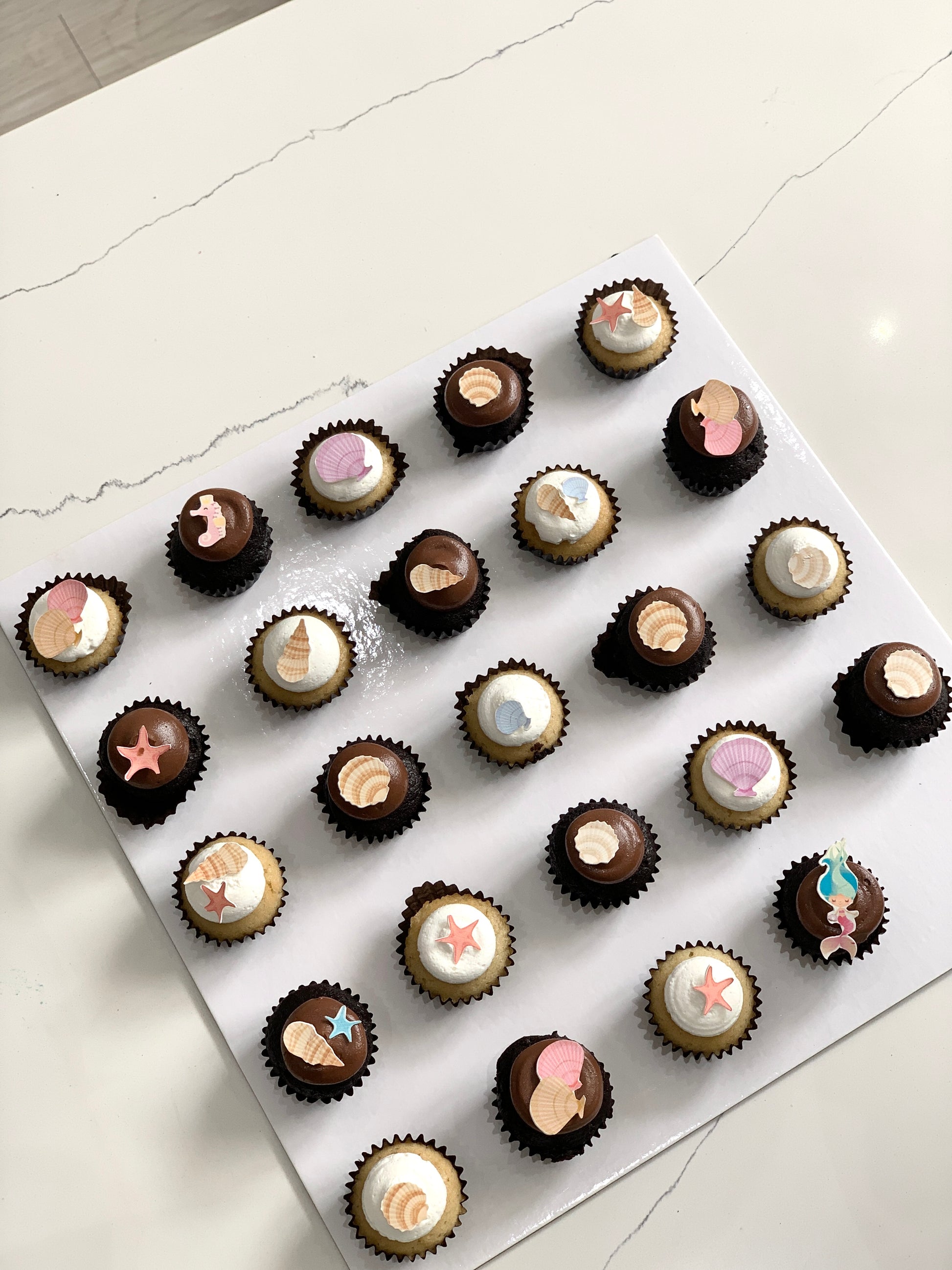Colorful cupcakes with swirled frosting and sprinkles from The Sinful Spoon on a white plate.