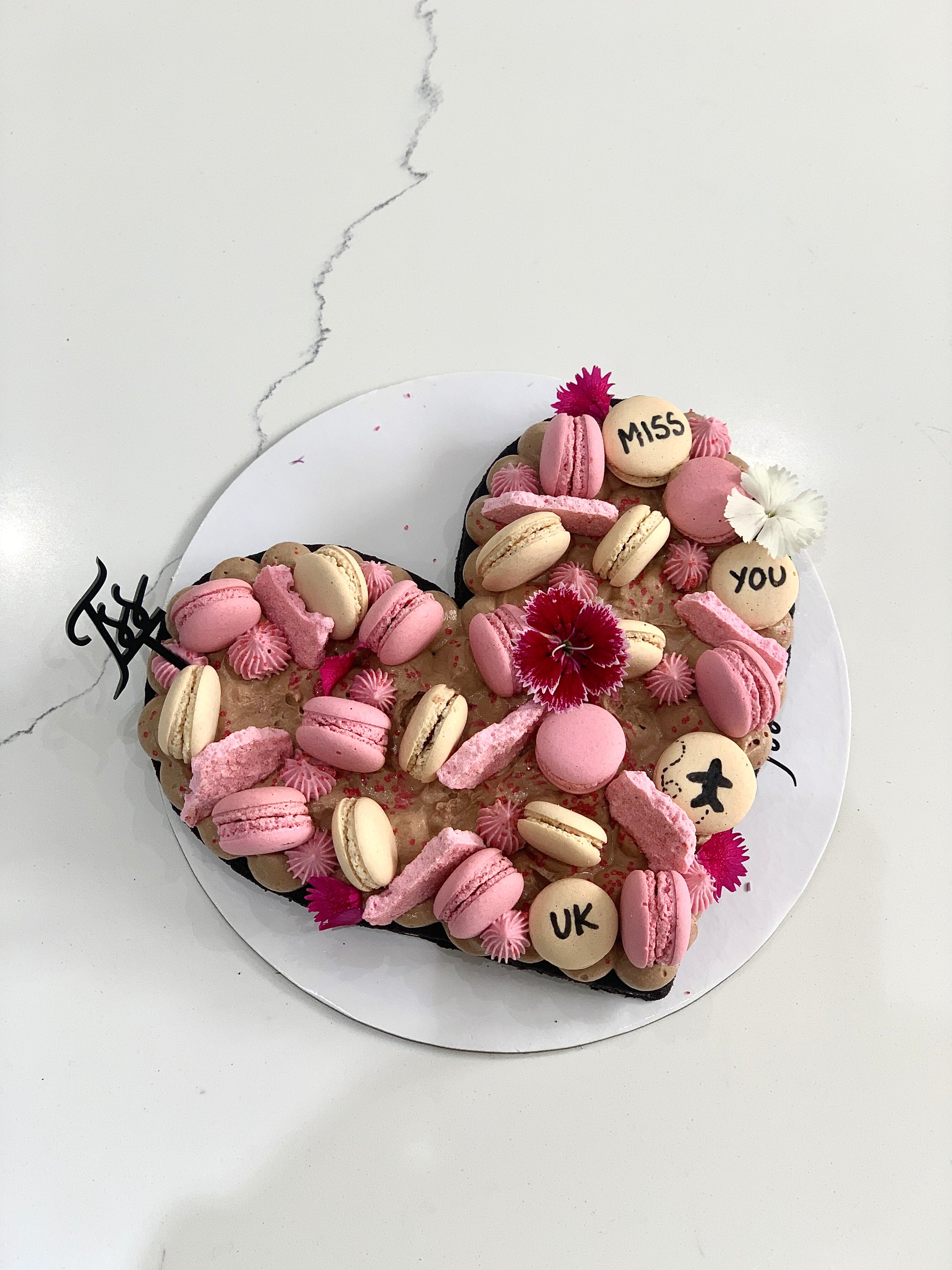 Valentine's Day cake from The Sinful Spoon with pink frosting, heart-shaped decorations, and floral accents on a white plate.