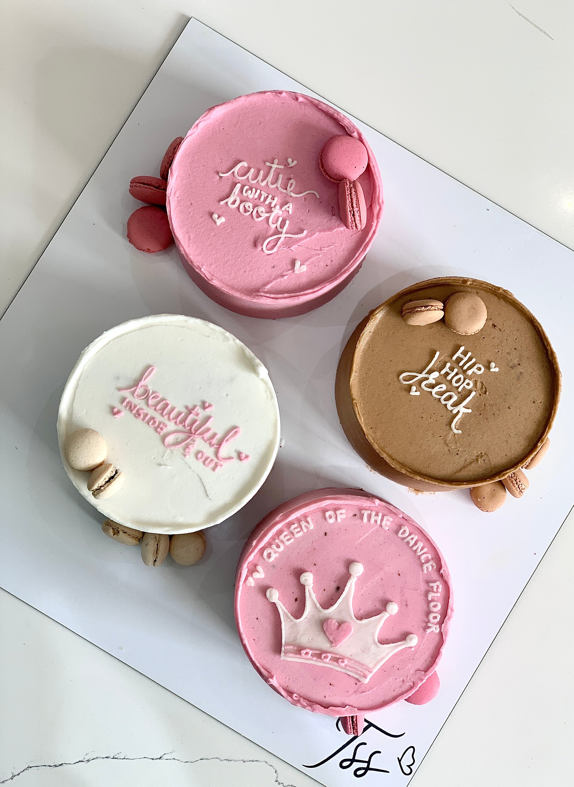 Colorful bento cakes from The Sinful Spoon with intricate designs and vibrant frosting, displayed on a white plate.