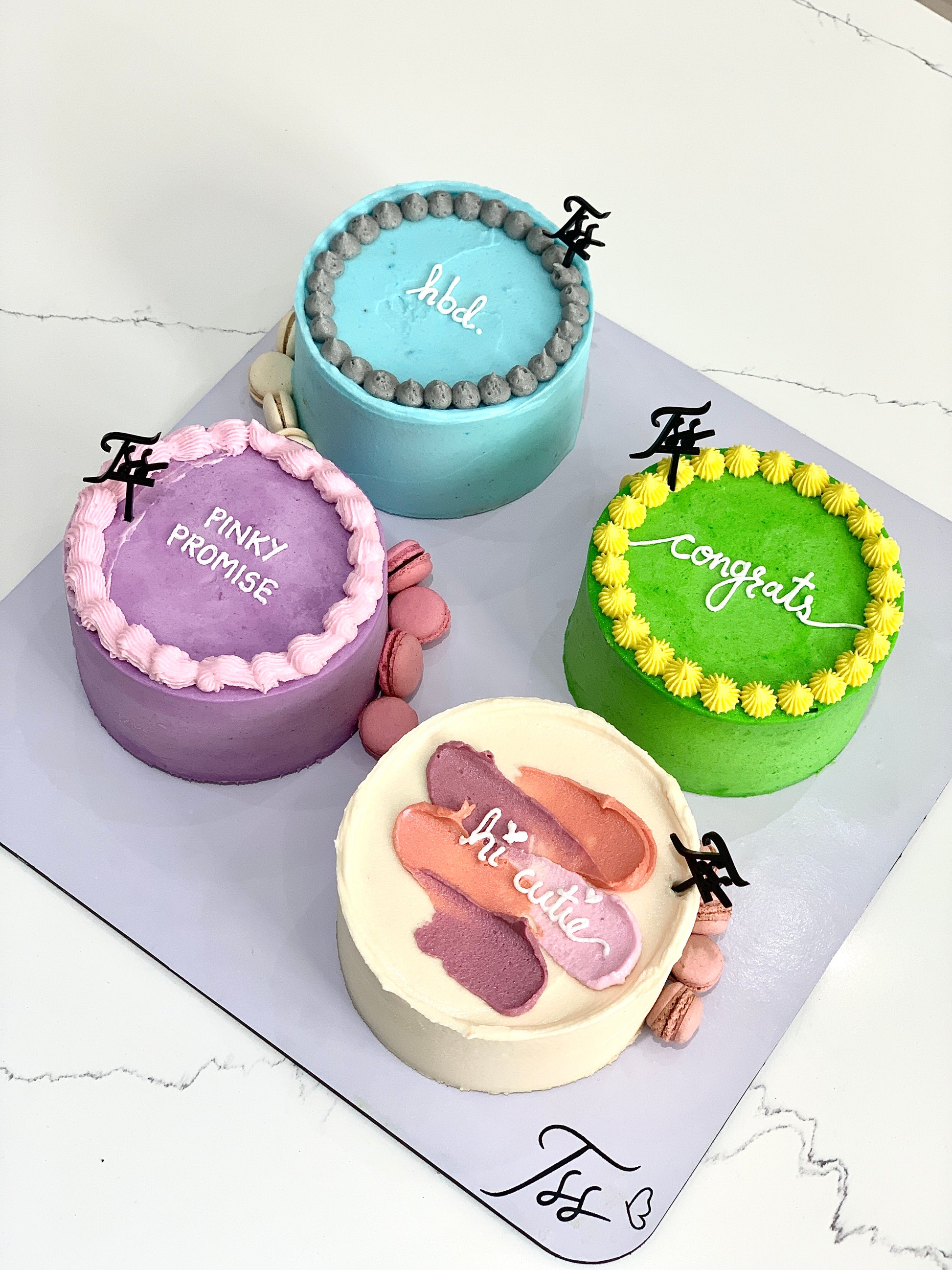 Assorted bento cakes from The Sinful Spoon with colorful designs and decorative toppings on a white plate.
