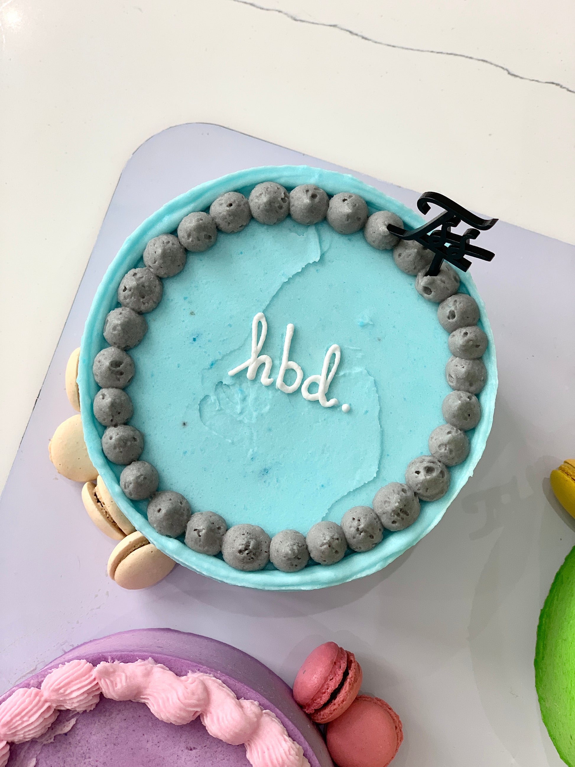 Colorful bento cakes from The Sinful Spoon with intricate designs and vibrant frosting, arranged on a white plate.
