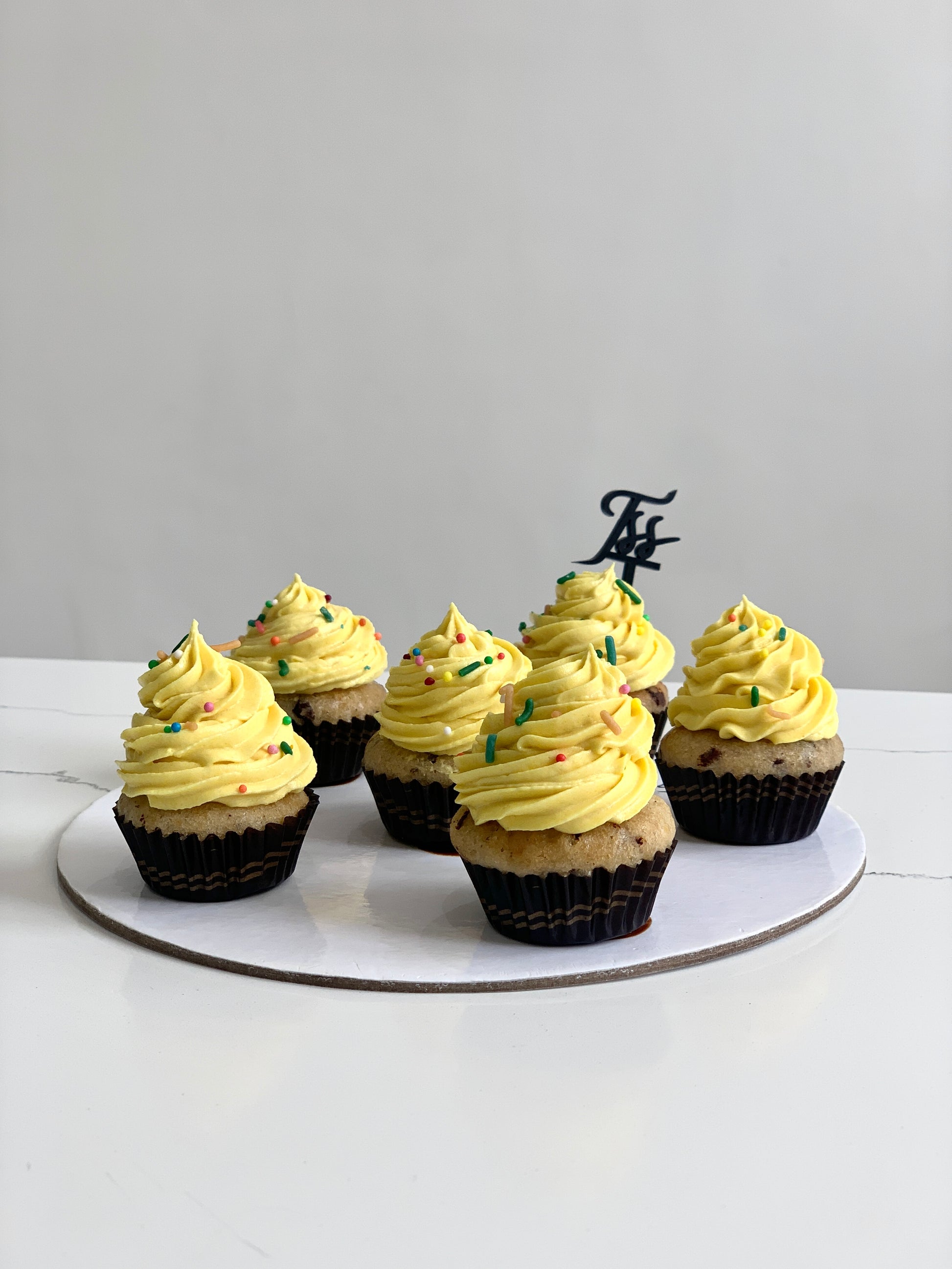 Decorative cupcakes from The Sinful Spoon with colorful frosting and sprinkles on a white plate, perfect for celebrations.