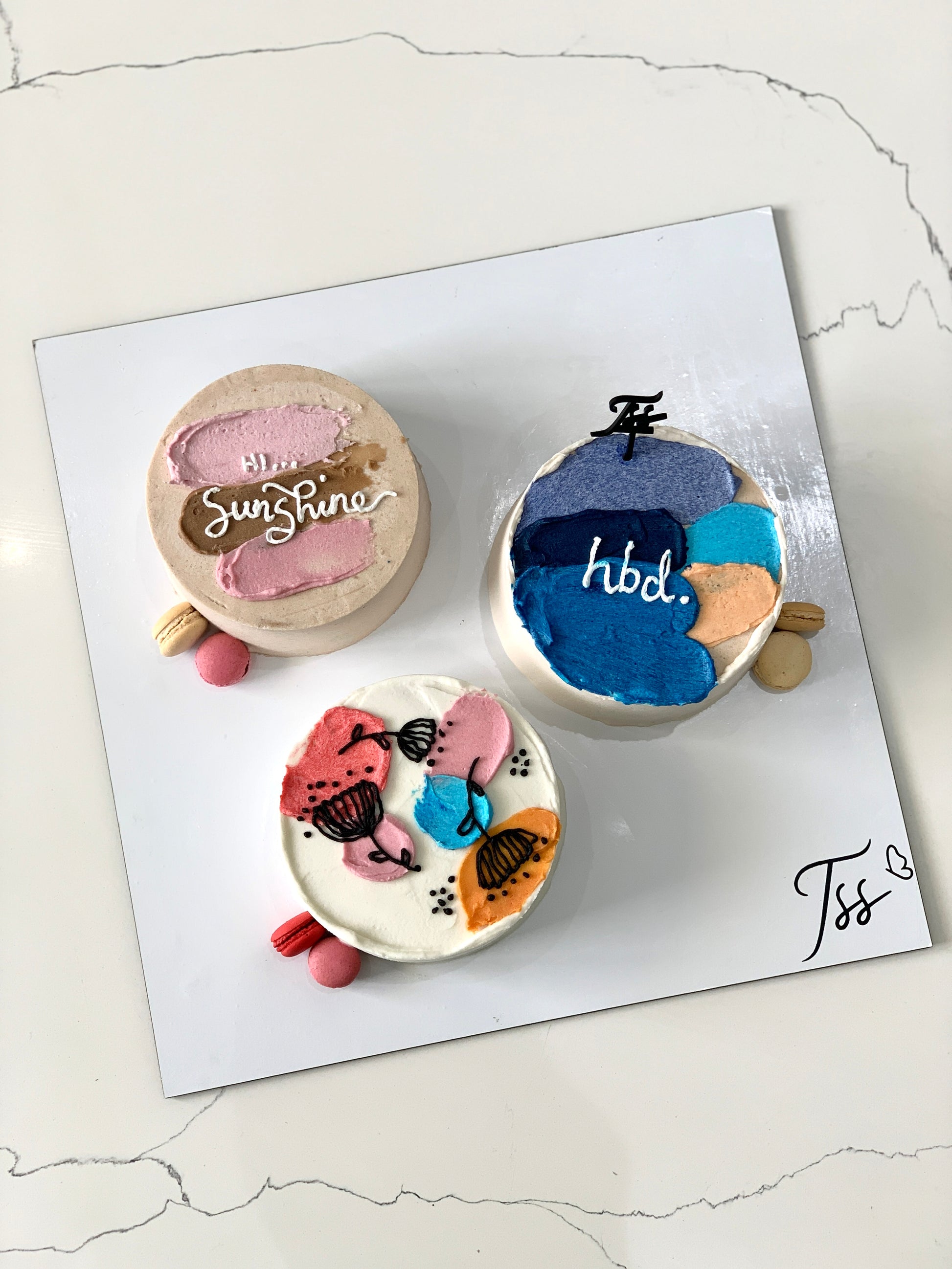 Assorted combo cakes from The Sinful Spoon with colorful frosting and decorative toppings, displayed on a plate.