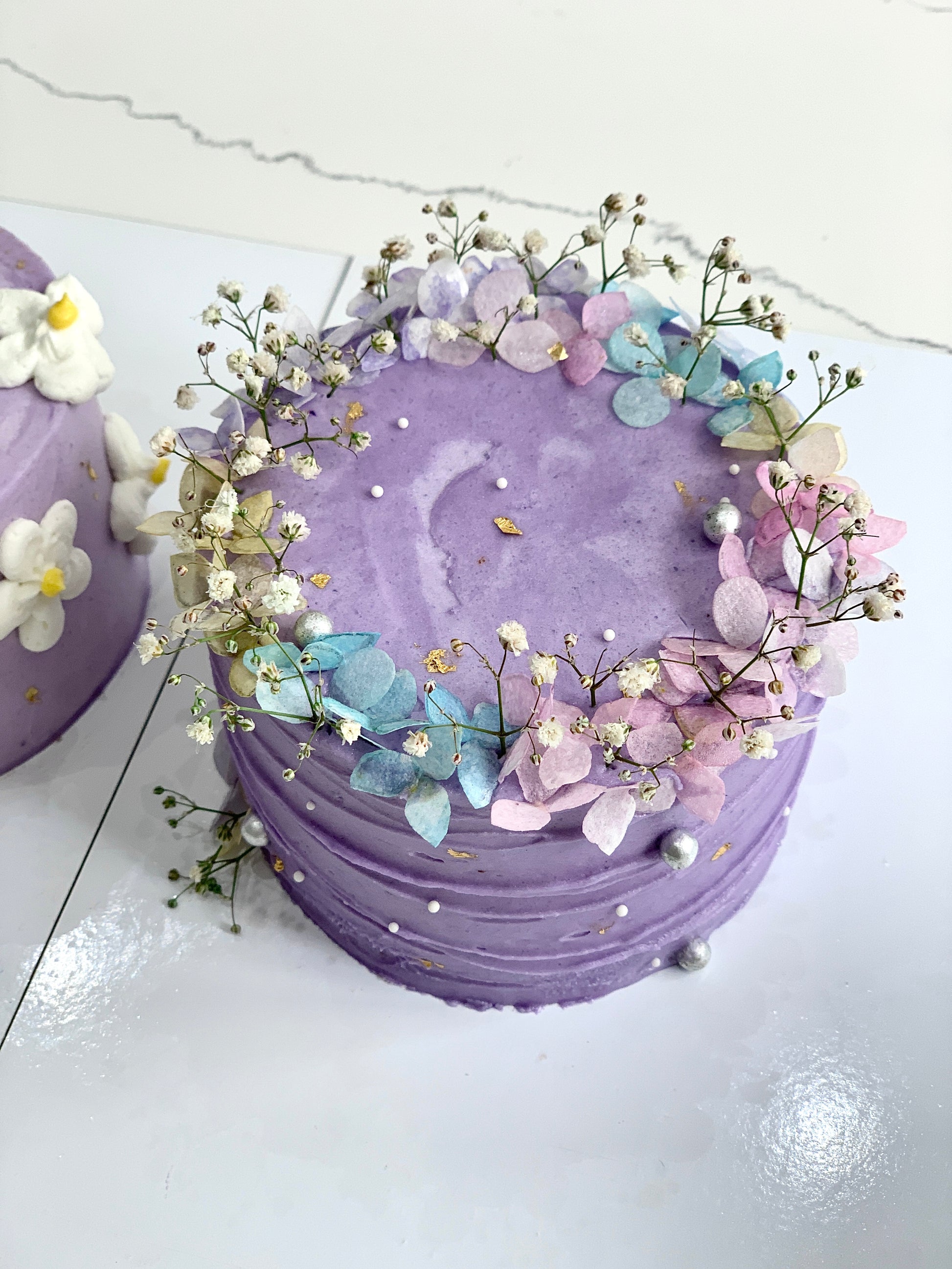 Decorative buttercream flower cakes by The Sinful Spoon with colorful, intricate floral designs on smooth cake surfaces.