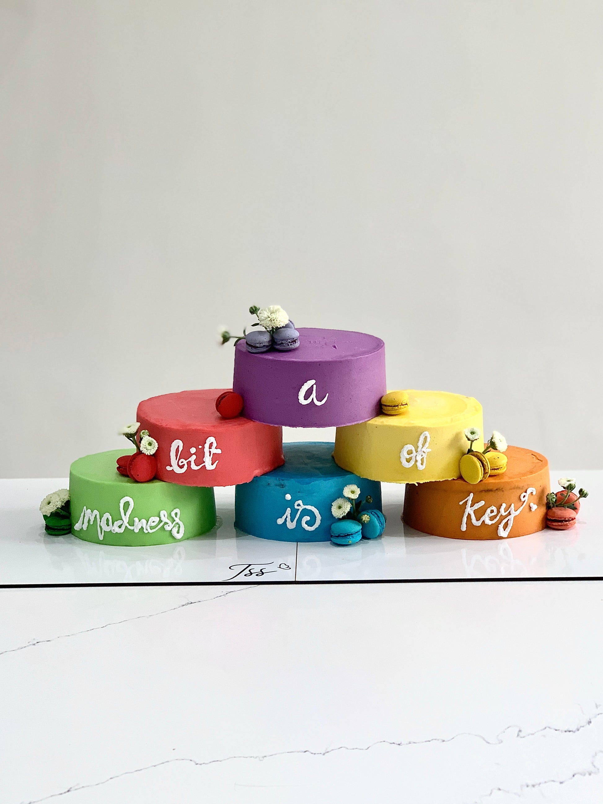 Layered cake tower by The Sinful Spoon with colorful frosting and decorative toppings, displayed on a cake stand.