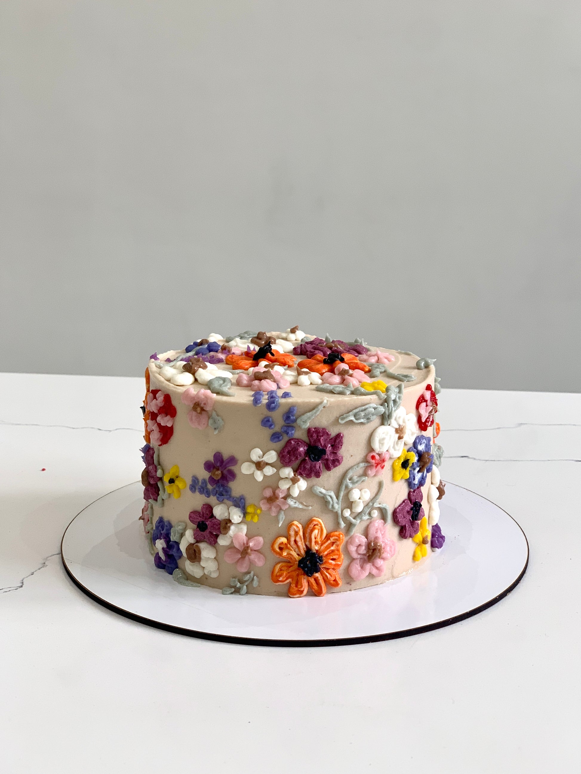 Decorative buttercream flower cakes from The Sinful Spoon featuring colorful, intricate floral designs on smooth cake surfaces.
