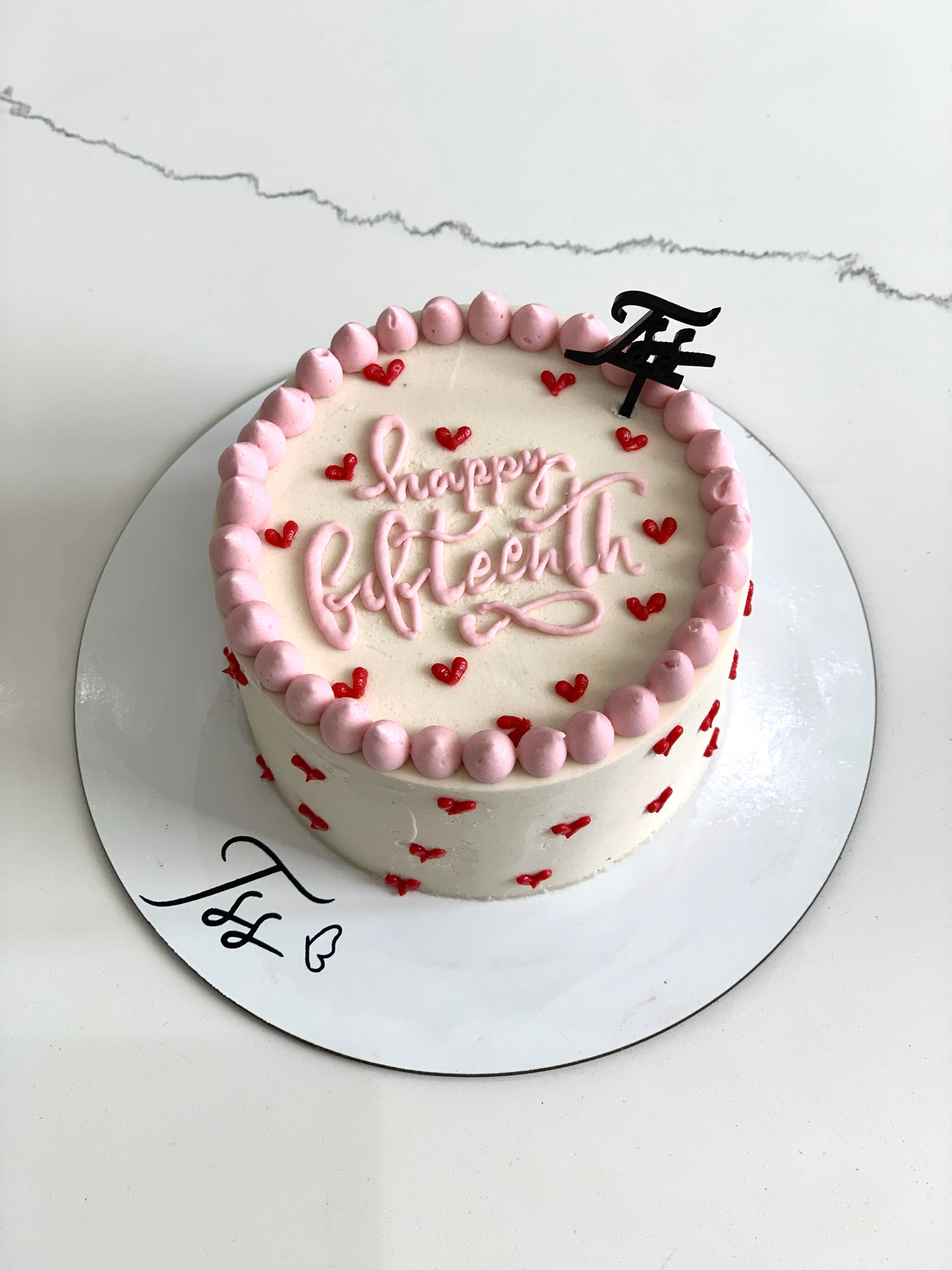 Valentine's Day cake from The Sinful Spoon with pink frosting, decorative hearts, and festive chocolate accents.