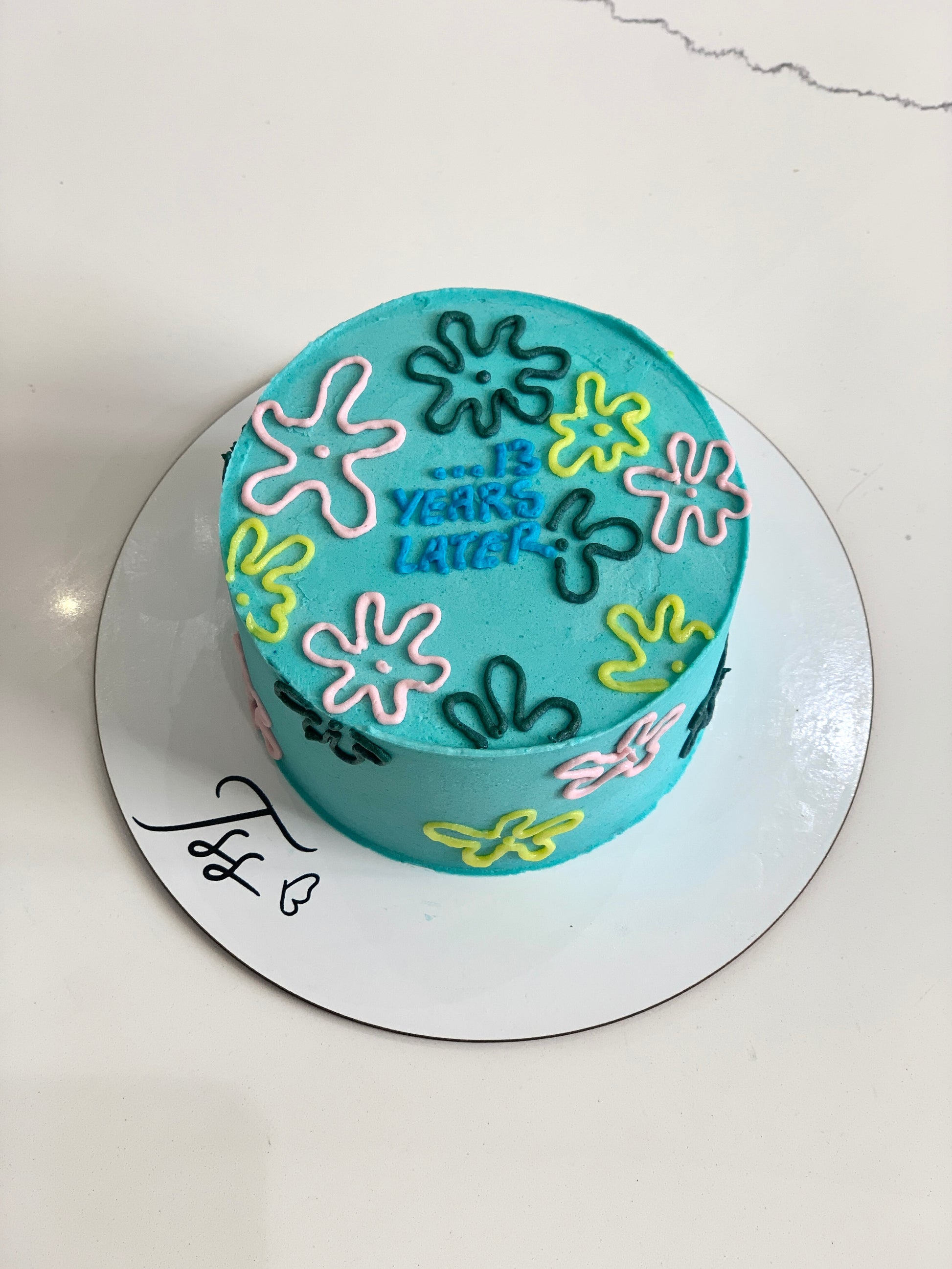 Decorative buttercream flower cake by The Sinful Spoon with colorful floral icing details on a white cake.
