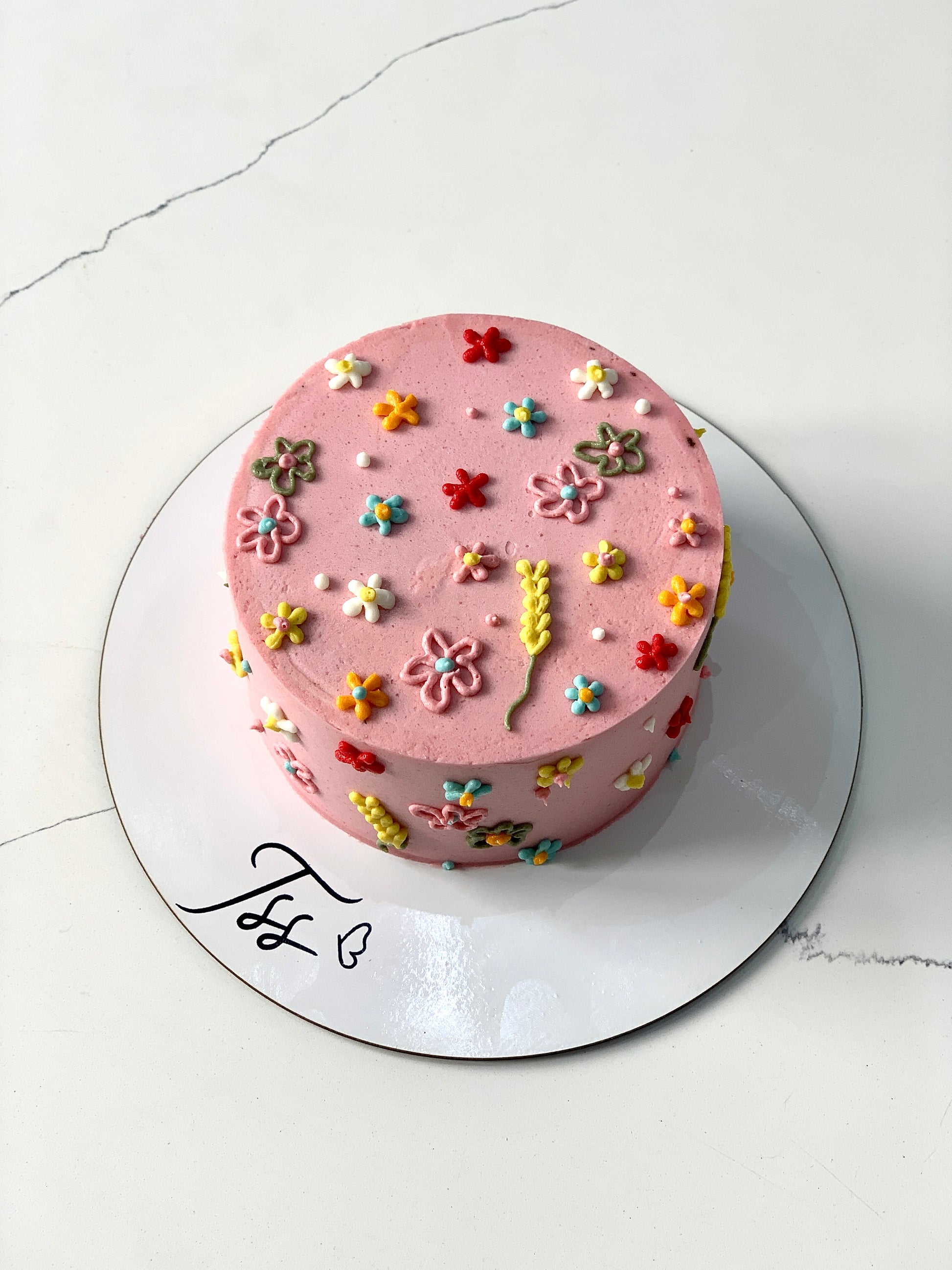 Decorative buttercream flower cakes with colorful floral designs on a white background, crafted by The Sinful Spoon.
